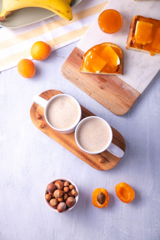 Colazione in cucina con due tazze appoggiate su un vassoio di legno, pane tostato e frutta sul tavolo