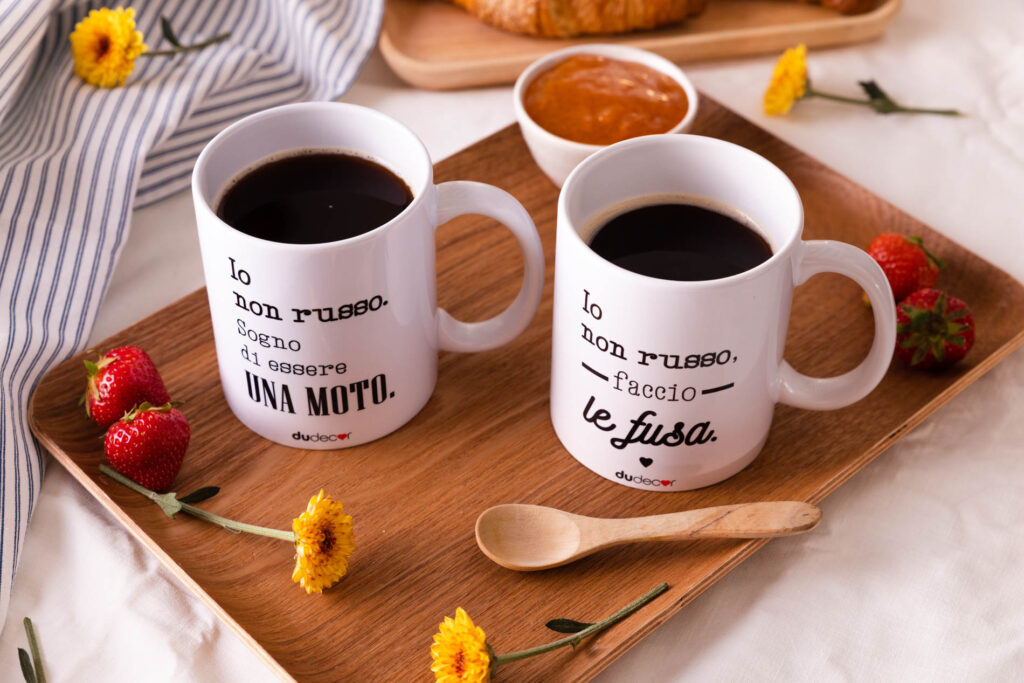 Due tazze di caffè su un vassoio in legno con frasi ironiche, fragole e fiori sul tavolo