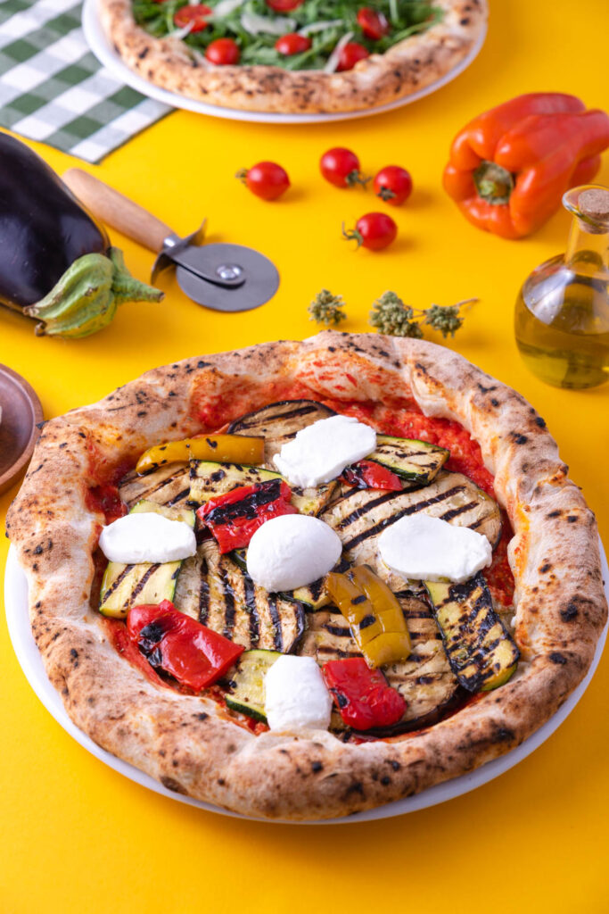 Pizza fatta in casa con verdure grigliate e mozzarella servita su piatto pizza in ceramica, con ingredienti freschi e taglia pizza su tavola colorata