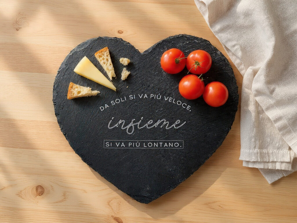 Tagliere a cuore in ardesia Dudecor su tavolo chiaro con pane spezzato, formaggio e pomodorini