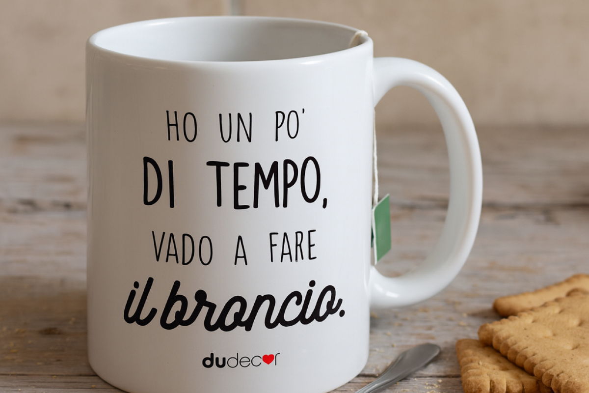 Tazza Dudecor “Ho un po’ di tempo, vado a fare il broncio” su tavolo di cucina con biscotti, briciole e cucchiaino.